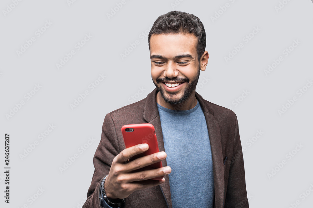 Wall mural portrait of handsome cheerful smiling young man using smartphone isolated on gray background. laughi