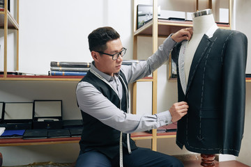 Mature Vietnamese tailor measuring suit jacket on mannequin