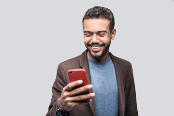 Portrait of handsome cheerful smiling young man using smartphone isolated on gray background....