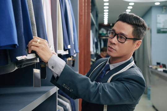 Shop assistant checking suits and jackets on rail in store