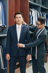 Naklejka na ściany i meble Menswear shop assistant helping middle-aged Vietnamese man to choose perfect suit