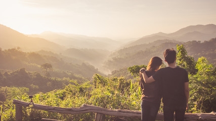 Fototapeta na wymiar Traveler hike and camping in summer concept, Back side of romantic Asian young couple see view sunrise and breathe fresh air top of mountain in tropical forest background.