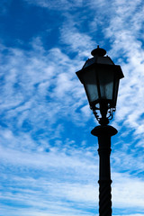 Fototapeta na wymiar Old iron street lamp with the winter blue sky with some clouds on the background, Siena, Tuscany, Italy