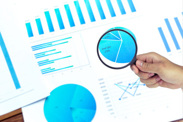 Businessmen use a magnifying glass to analyze the company's data and statistics from the chart.