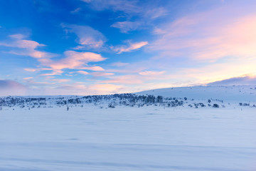 Arctic landscape. Pink clouds against a clear blue sky as the sunset approaches over a snow covered landscape