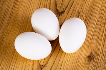 Three white chicken eggs on a wooden board