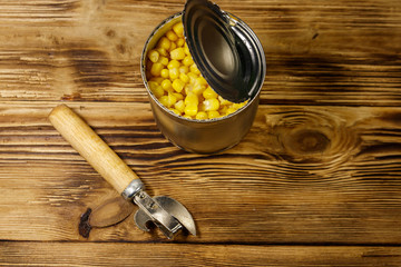 Open tin can of corn and can opener on wooden table