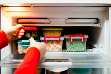 Woman placing container with frozen mixed vegetables in refrigerator.