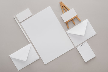 flat lay with white empty papers and letters with toy easel at workplace on grey background