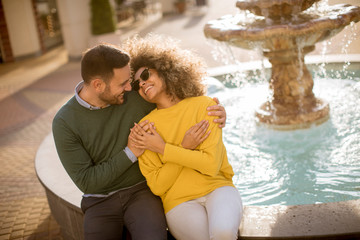 Beautiful smiling love couple sitting near fountain on a sunny day