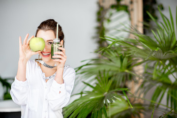 Portrait of a young woman with apple and smoothie drink indoors. Healthy eating and wight loss...