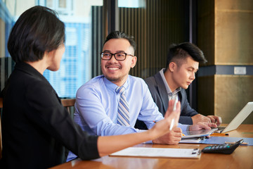 Smiling Asian businessman talking to his female coworkers about company development