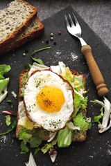 Bran toast with salad mix and fried egg on top. Healthy breakfast presented on a stone board. Keto diet. Keto breakfast or snack.