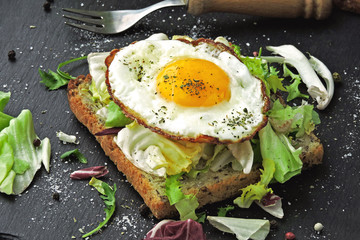 Bran toast with salad mix and fried egg on top. Healthy breakfast presented on a stone board. Keto diet. Keto breakfast or snack.
