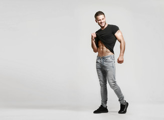Muscular model sports young man in blue jeans raised his hand t-shirt and showing his press on a...