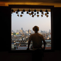 A young man looks at the city of Bangkok from the window