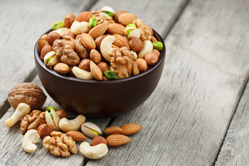 Wooden bowl with mixed nuts on a wooden gray background. Walnut, pistachios, almonds, hazelnuts and cashews, walnut.