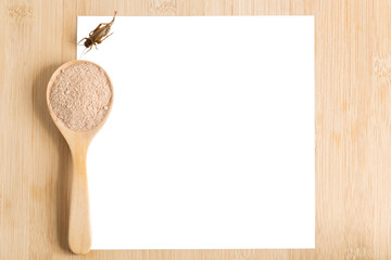 Cricket powder insect for eating and cooking food in wooden spoon with white paper mockup on wood background it is good source of protein edible for future food. Entomophagy concept. Top view.