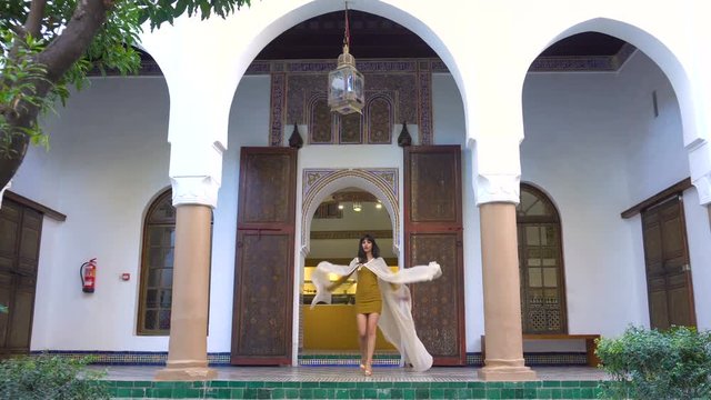 Beautiful Moroccan Girl Waving her white mantle in Picturesque Dar Si Said Riyad in Marrakech at sunset time