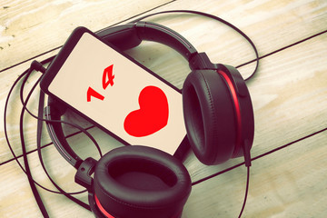 black headphones with smartphone on a light wooden background, on the smartphone screen love symbol in the form of a heart,  Valentine's day holiday