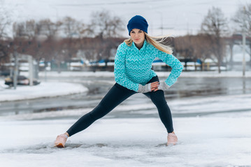 woman stretches her legs before jogging in the city in winter