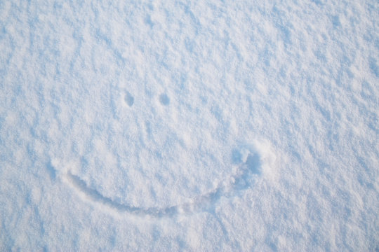 Smiling face drawn on white, fluffy snow, winter frosty evening. Close-up.