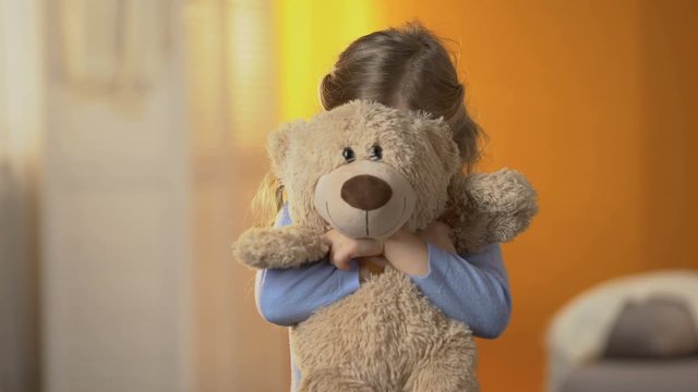 Preschool shy girl hiding behind teddy bear, childish psychological problems