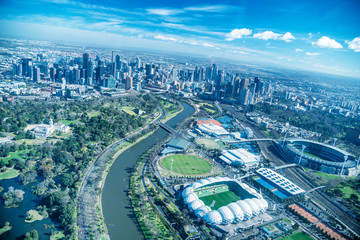Naklejka na ściany i meble MELBOURNE - SEPTEMBER 8, 2018: Aerial view of city skyline and stadiums from helicopter. Melbourne attracts 15 million people annually