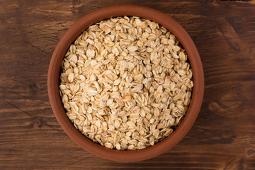 Rolled oats or oat flakes in bowl on wooden background. Healthy lifestyle, healthy eating concept. Top view