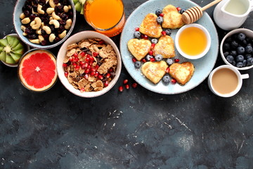 Brunch or breakfast concept on dark background. Valentine's Day or Mather's Day. Healthy breakfast fried eggs, salad, pancakes, juice, coffee, granola and dried fruits. Top view with copy space.