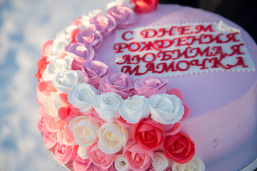Beautiful cake with pink flowers in the hands of a girl on a background of snow. The inscription on the cake, translated from Russian: Happy Birthday, my dear mommy!
