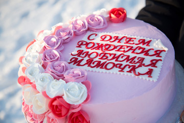 Beautiful cake with pink flowers in the hands of a girl on a background of snow. The inscription on...