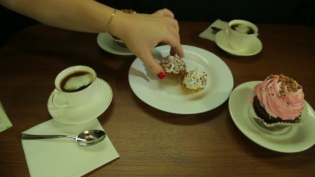 Female hand puts cakes in a white plate to coffee. The average plan