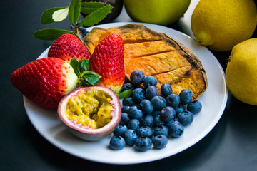 Vegan breakfast: variety of fruits, nuts and berries on the grey wooden table, selective focus; fruit salad