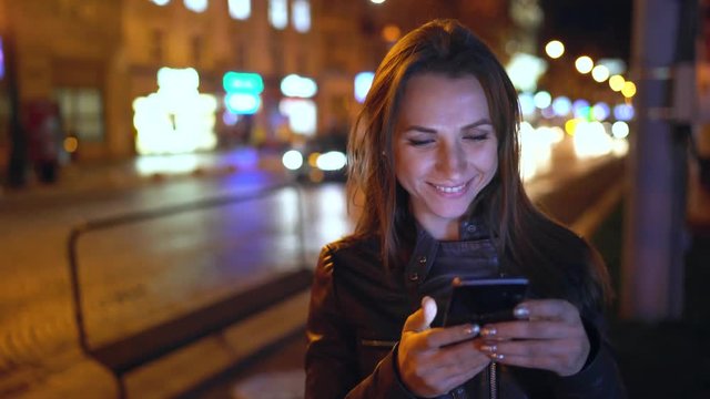 Attractive woman using a smartphone while walking through the streets of the evening city