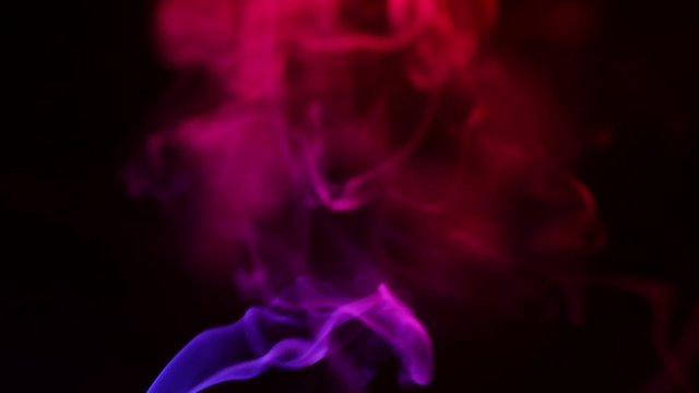 Multicolored smoke from aromatic sticks close up on black background
