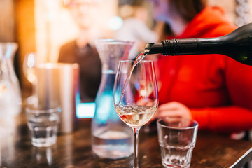 Waiter pouring wine in glass for guests at table in bar restaurant party