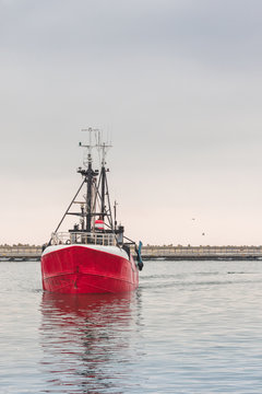 Red fishing vessel swimming in the dock and its reflection in water