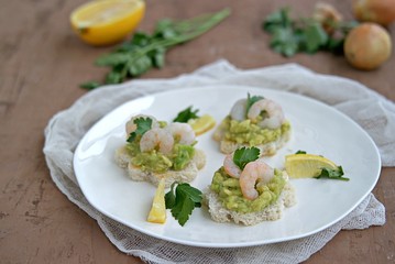 Small snack sandwiches on white bread with guacamole and shrimps on a white plate. Selective focus.