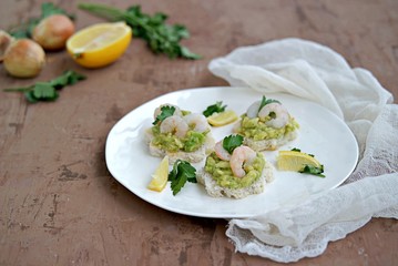 Small snack sandwiches on white bread with guacamole and shrimps on a white plate. Selective focus.