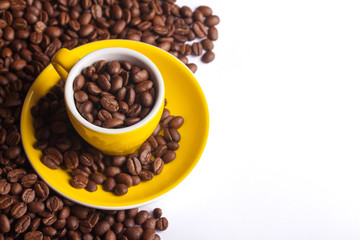 Empty copy space morning coffee background. Yellow espresso cup filled with brown coffee seeds, Raw and fresh coffee beans in studio isolated on white.