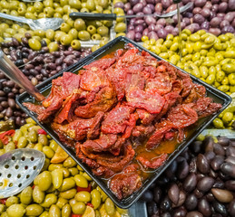 Pile of dried tomatoes with background of different pickles and olives, Mediterranean market