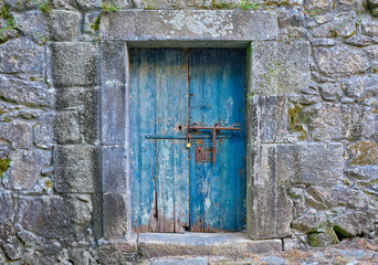 Rustic old blue wooden door, locked, showing aging and wear and tear on old stone building