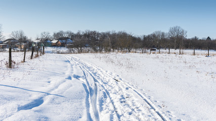 Fototapeta premium Road along the snow-covered fields to the village, winter time
