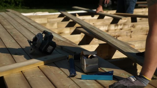 Static shot, of a carpenters, working on adjusting and placing deck boards, on a terrace. on a sunny summer day, in Norway