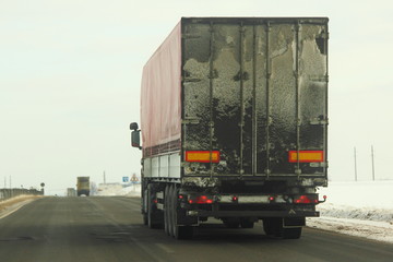 Rear view on dirty european semi-trailer truck on asphalt winter road - business, leasing