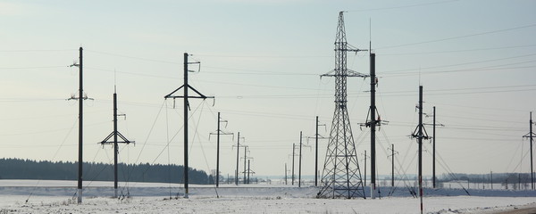 Masts of an air power line, power substation in the winter on the snow-covered field - traditional energy, electricity, electric power