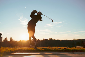 Young junior golfer practicing in a driving range with beautiful sunset light in winter. - Powered by Adobe