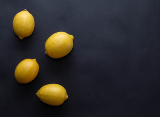 four yellow lemons on a dark black background