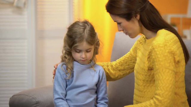 Young female comforting little daughter, touching girls face tenderly, closeness